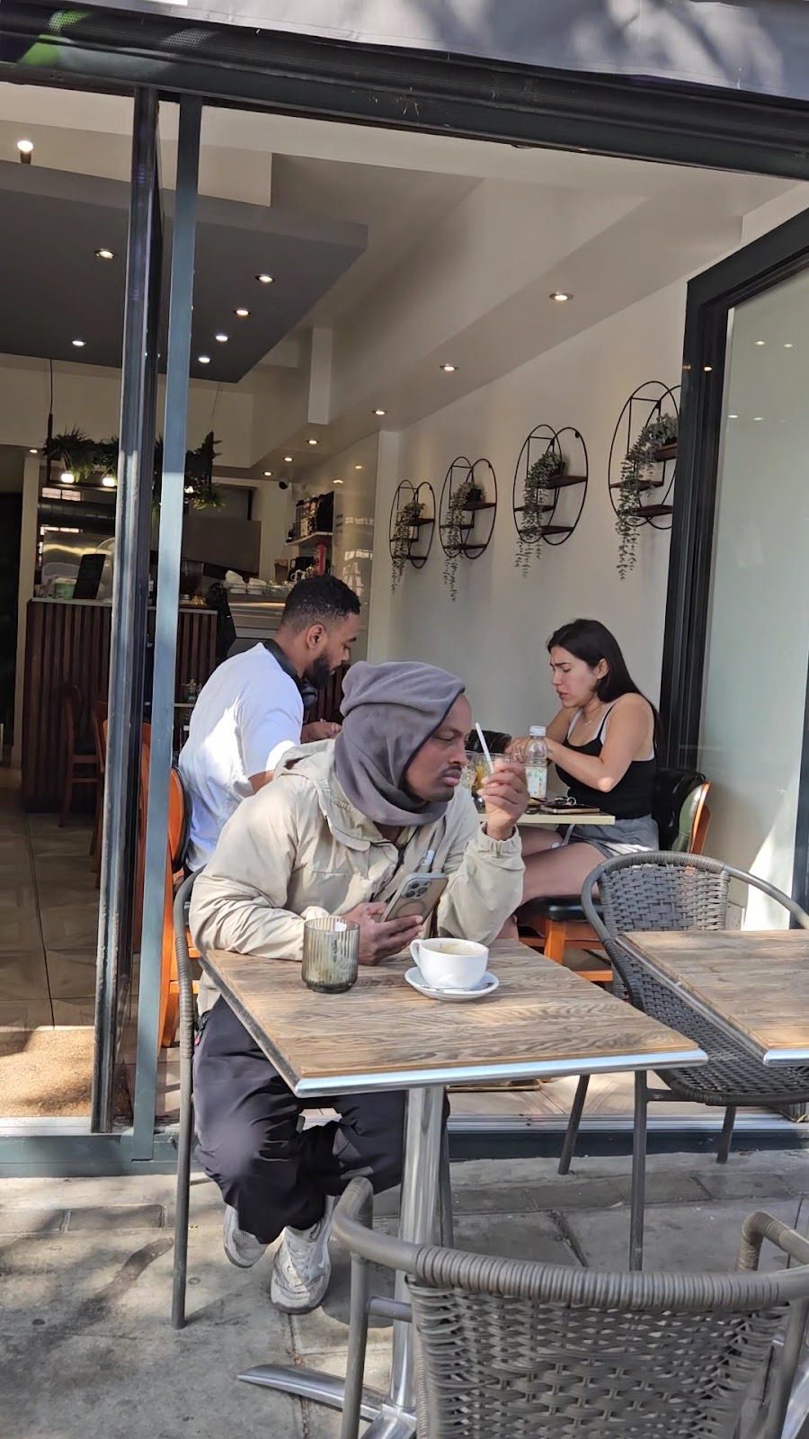 Customers sitting at a table with coffees, seen through the open front of the cafe