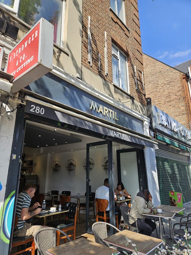 Street-level exterior of 280 Norwood Road with the dark navy awning, pavement tables and customers outside on a bright day