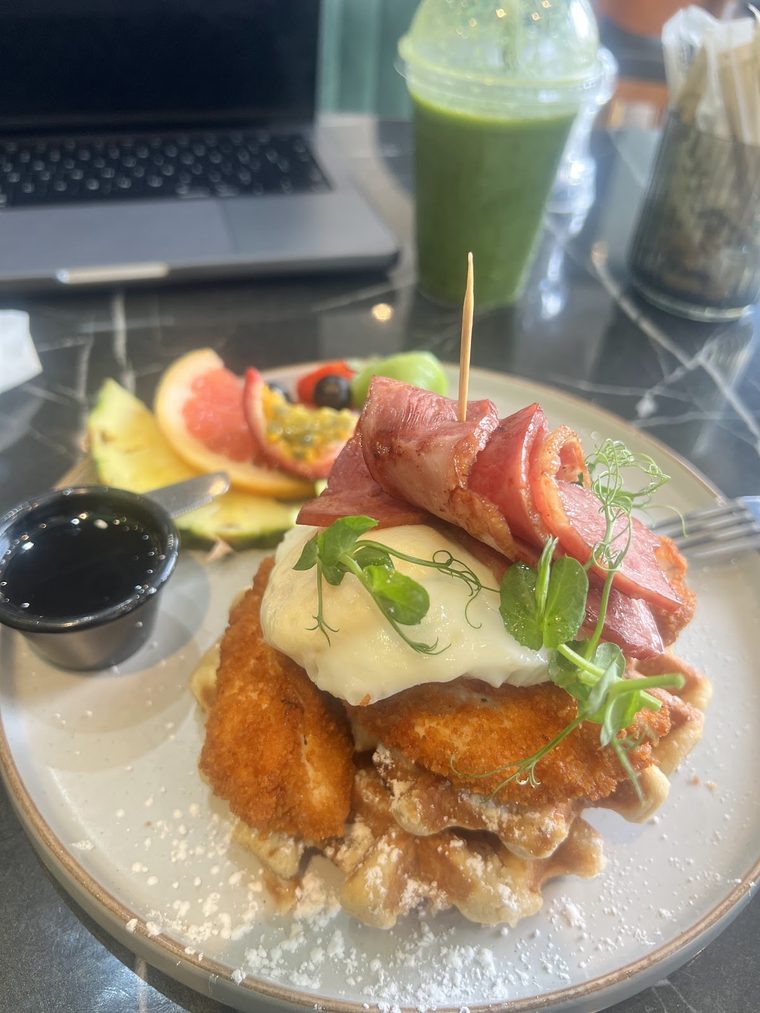 Chicken and waffles stacked with a poached egg and bacon, dusted with icing sugar