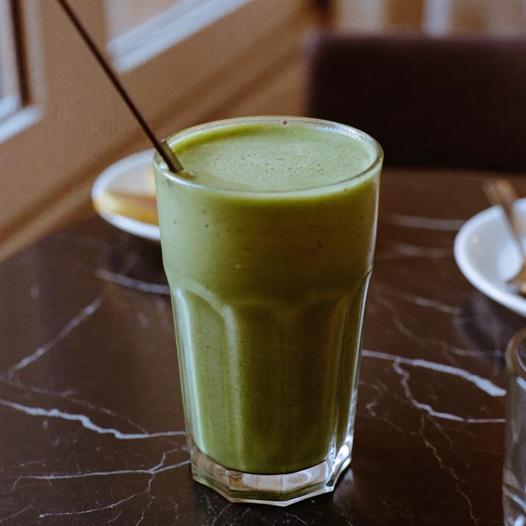 A tall glass of green smoothie on a black marble table