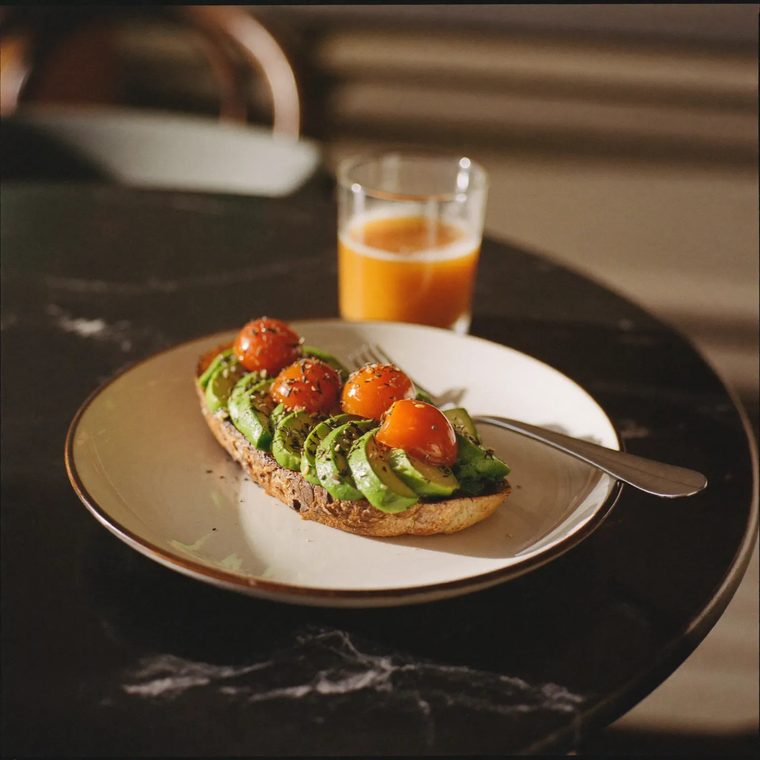 Avocado on toasted sourdough with tomatoes on a white plate